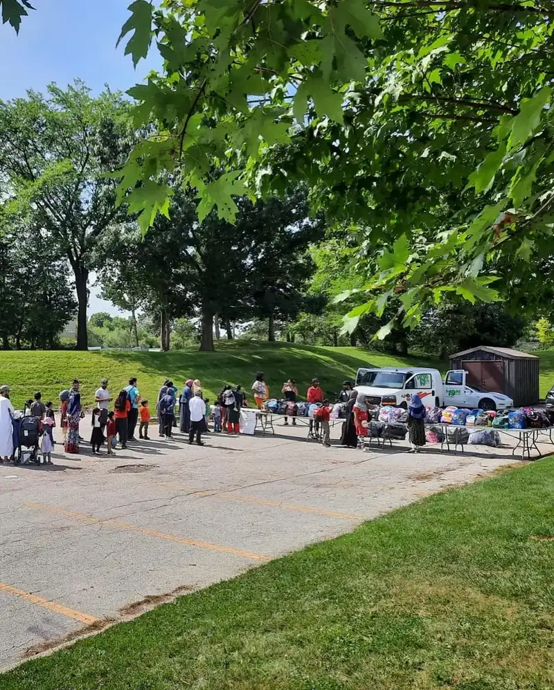 Families lined up at outdoor tables stacked with backpacks at the Back to School BBQ