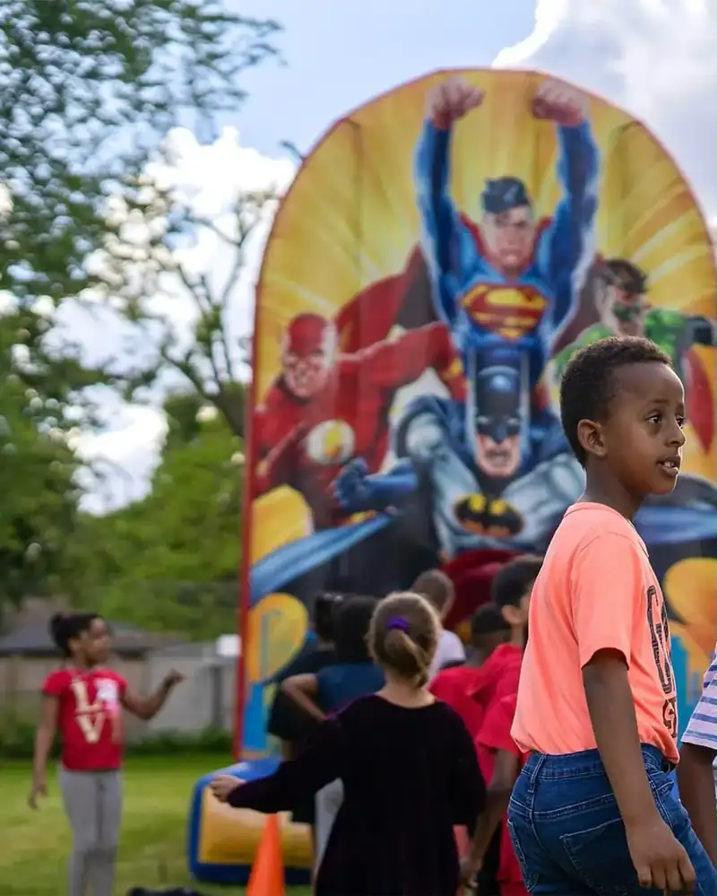 Children gathered around a superhero inflatable at an outdoor school carnival