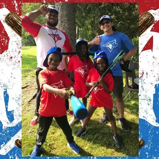 Three youth in Blue Jays shirts holding bats, posing with their coaches on a grass field