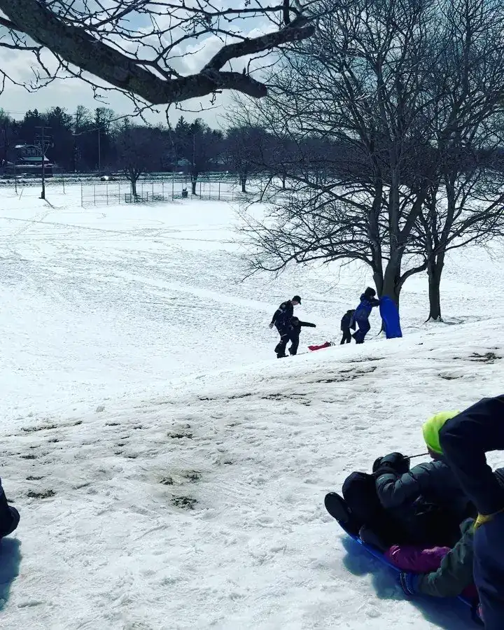 Children sledding down a snowy hill while community officers look on