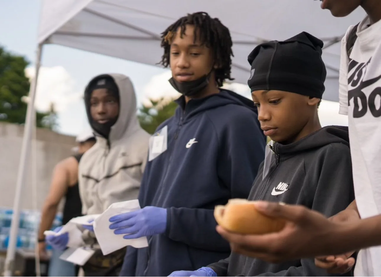 Good Guide Ambassadors in gloves serving food under a canopy at a community barbecue in Scarborough