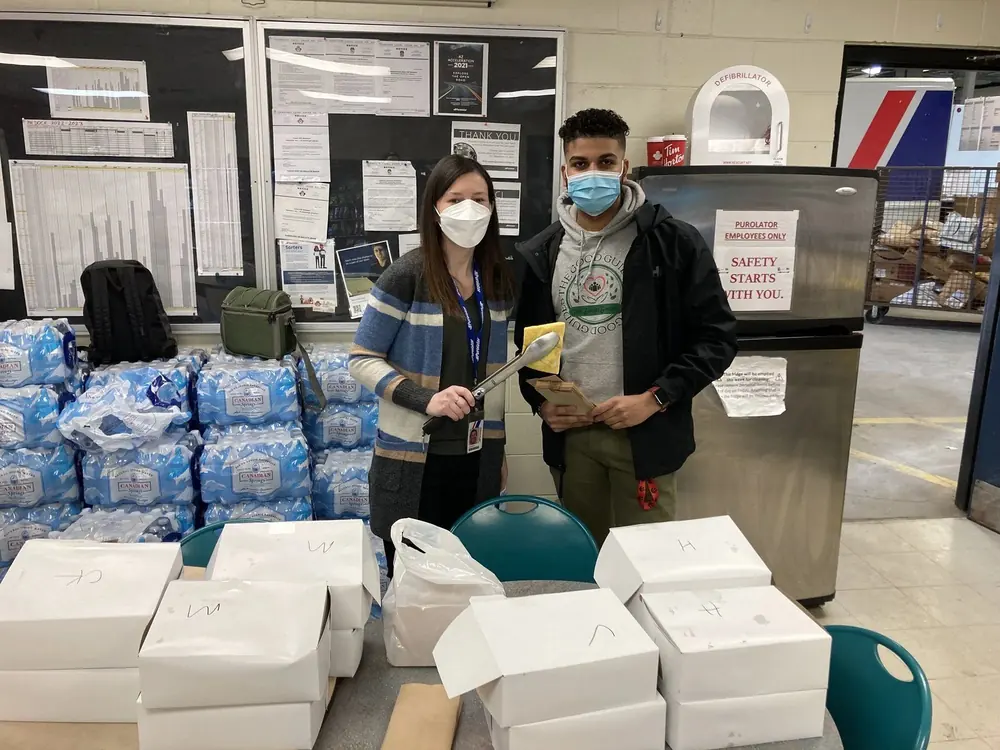 Good Guides youth and a partner staffer packing meal boxes and bottled water for a community distribution