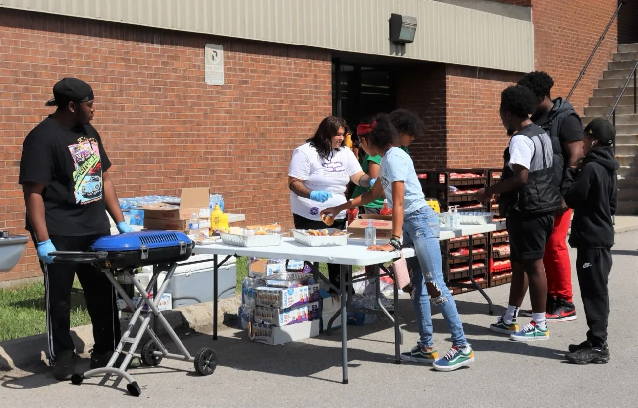 Neighbours and young people gathered around a serving table at a Good Guides community barbecue in Scarborough
