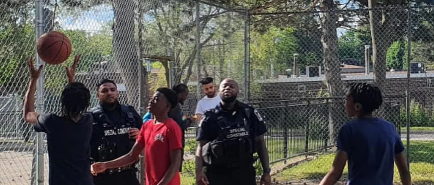 Young people playing basketball on an outdoor court with Toronto Police Service special constables